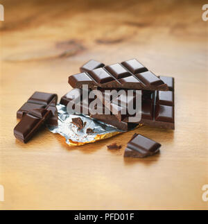 Barra di cioccolato fondente quadrati suddivisi in grossi pezzi impilati nella parte superiore di ogni otherover lamina di alluminio e singoli quadratini, vista frontale. Foto Stock