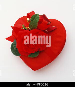 Presente nel cuore-scatola sagomata avvolto in carta rossa, rosso e oro nastro decorato con artificiali rose rosse e foglie, vista frontale. Foto Stock