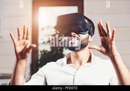Multiculturale uomo barbuto che indossa la realtà virtuale gli occhiali e guardare video in appartamento moderno Foto Stock