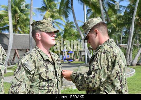 KWAJALEIN, Isole Marshall (giugno 7th, 2018) Ensign Daniel Hulse, destra, dirigente, Naval Mobile Battaglione di costruzione (NMCB) 11, Costruzione Civic Dettaglio azione Isole Marshall, premi Hospital Corpsman 3rd Class Andrew Carr, assegnata anche a NMCB-11 CCAD Isole Marshall, il suo Marine Expeditionary Warfare pin. NMCB-11 è distribuito per eseguire la costruzione, umanitari e di assistenza estera, il teatro e la cooperazione in materia di sicurezza nel VII flotta area di operazioni. Foto Stock