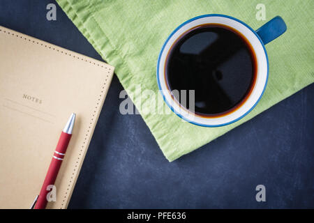 Ottenere pronto a scrivere con un caffè e un notebook con un tovagliolo verde su un gesso nero superficie. Foto Stock