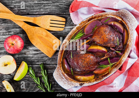 L anatra arrosto gambe cotto al forno con vino rosso e rosmarino e la scorza di arancia e fette di mela in posizione gratin piatto, stelle di anice e mela verde su bianco peelin Foto Stock