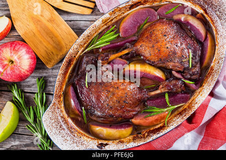 L anatra arrosto gambe cotto al forno con vino rosso e rosmarino e la scorza di arancia e fette di mela in posizione gratin piatto, stelle di anice e mela verde su bianco peelin Foto Stock