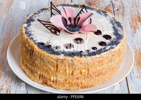 Lussureggianti di semi di papavero, noci e uvetta pan di spagna con strati di crema e decorate con gocce di cioccolato e lo zucchero a velo fiore rosa sul piatto bianco, Foto Stock