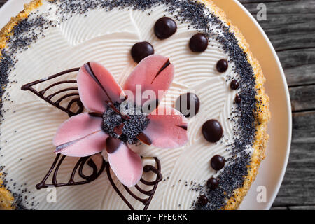 Lussureggianti di semi di papavero, noci e uvetta pan di spagna con strati di crema e decorate con gocce di cioccolato e lo zucchero a velo bellissimo fiore rosa su w Foto Stock