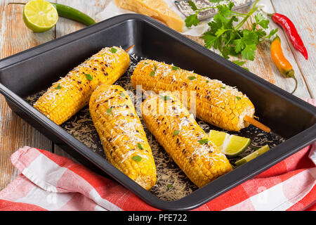 Mais alla griglia su cob cosparso con il prezzemolo e il parmigiano grattugiato e fettine di lime nel piatto di torrefazione con carta asciugatutto, peperoncino semi di limone Foto Stock