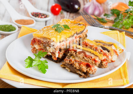 Porzione di deliziosa moussaka stratificata decorate con prezzemolo tagliato a fettine cotta per autentica ricetta, su vassoi con igienico, su bianco peeling pa Foto Stock