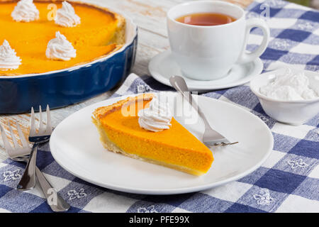 Fetta di torta di zucca - dessert tradizionale per la cena di gala, decorata con panna montata, con tutta la torta, piccola ciotola con la panna montata e la tazza di Foto Stock