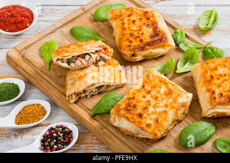 Fried flatbread avvolge farcite con carne di pollo, cetriolo, coleslaw, Pomodoro ,spinaci, aneto sul tagliere con il sugo di pomodoro e le spezie su porcellana cucchiai Foto Stock