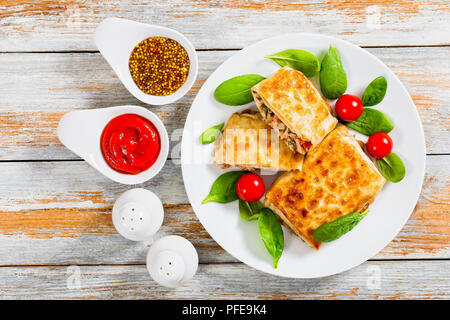 Fritti involtini di focacce ripiene di carne sul piatto bianco fresco con le foglie di spinaci e i pomodori, il sale e il pepe, ketchup e senape francese in g Foto Stock