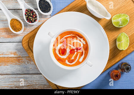 Thai zuppa di zucca purea con rosso pasta tailandese, latte di cocco e panna in tazza bianca sulla piastra sul tagliere con il peperoncino e salse di pesce in bottiglia Foto Stock