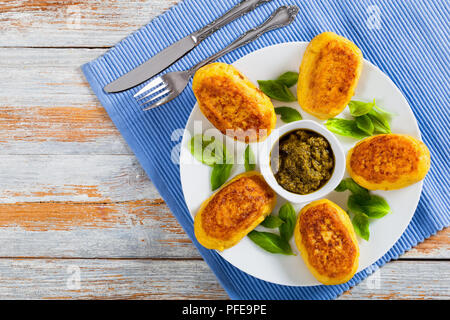 Purea di deliziose frittelle di patate con la massa di pollo ripieno di carne sul piatto bianco con salsa di pesto in salsiera sulla tabella MAT con coltello e forchetta, vista Foto Stock