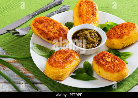 Italian frittelle di patate da purea di patate con salsa di pesto e foglie di basilico bianco sul piatto sul tavolo verde mat, close-up vista da sopra Foto Stock