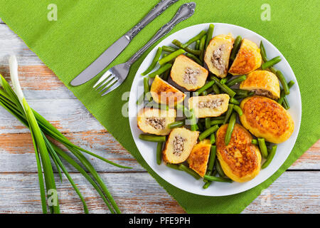 Deliziose frittelle di patate da purea di patate riempito con terra carne di pollo con fagiolini sul piatto bianco, cipollina su sfondo, Foto Stock