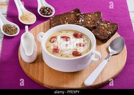 La birra e il Cheddar minestra in crema con salsiccia Kielbasa cosparso di cumino in bianco coppa zuppa sul bordo rotondo con pane di segale con semi, close-up, vista dal Foto Stock