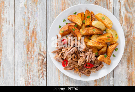 Porzione di tirata slow-cotta deliziosa carne arrostita al forno con patate fritte cunei cosparsa di prezzemolo sulla piastra bianca con spezie e peperoncino su Foto Stock