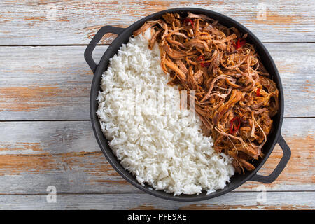 Tirato slow-cotto spalla di maiale grigliato in forno con riso basmati in ferro padella sul tavolo di legno, vista da sopra Foto Stock