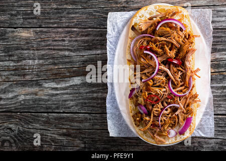 Grigliata di carne di maiale tirato la ciabatta Sandwich Aperto con BBQ SAUCE, cipolla rossa e peperoncino su carta pergamena sulla targhetta ovale, copyspace sinistra, vista dal abo Foto Stock