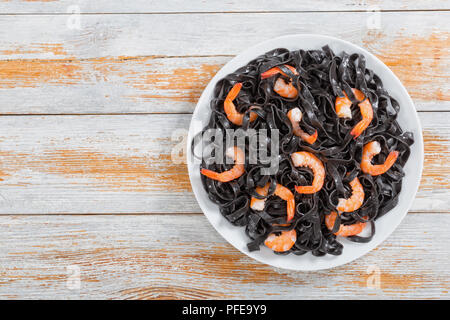 Deliziosa nero di seppia pasta con gamberi sulla piastra bianca su vecchie tavole di legno, vista da sopra