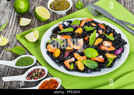 Tagliatelle nere con insalata di gamberetti, cozze, fresco verde spinaci, lattuga, rucola sul piatto bianco sulla tabella mat on dark tavolo in legno con fettine di lime e s Foto Stock