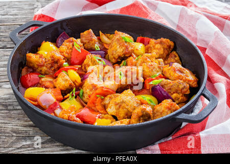 Dolce e aspro fritto pezzi di carne di maiale con verdure, cosparsi di cipolla verde nella casseruola di ferro sul legno scuro sfondo, cinese tradizionale ricetta, c Foto Stock