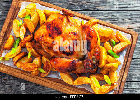 Dorate e croccanti della pelle di pollo grigliato in forno con spicchi di patate e porri sul tagliere in legno vecchio tavolo scuro,vista da sopra Foto Stock