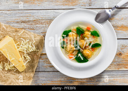 Deliziosi piatti della cucina italiana wedding zuppa con polpette di carne, pastina risini,gli spinaci e le verdure in bianco bordo larga ciotola e un pezzo di formaggio parmigiano su parchmen Foto Stock