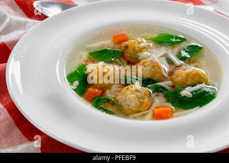 Una deliziosa zuppa di nozze con polpetta, carote e spinaci in bianco bordo larga ciotola con cucchiaio sulla tovaglia, autentica ricetta, close-up Foto Stock