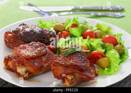 Gustose grigliate di cosce di pollo con fresco verde insalata di lattuga, cetriolo, olio d'oliva e pomodori sul piatto bianco, i semi di zucca condimento di olio nel sugo boa Foto Stock