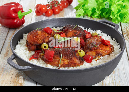 Riso con grigliate di cosce di pollo, il peperone rosso, verde oliva e rosmarino in ghisa faitout su bianco vecchio tavolo in legno, verdure e lattuga su Foto Stock