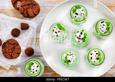 Porzioni di menta Mousse Cheesecake conditi con panna montata, scaglie di cioccolato e foglie verdi in Dessert le coppe di vetro con tartufo e i cookie su pape Foto Stock