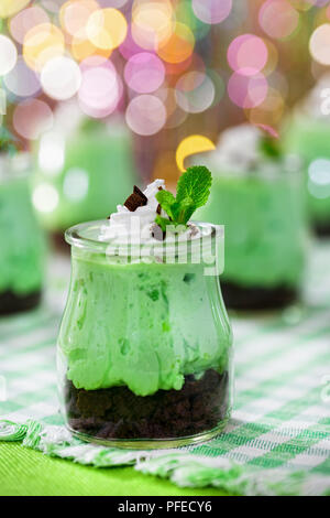 I kiwi Mousse Cheesecake dolce conditi con panna montata e scaglie di cioccolato in bicchieri di vetro sul vecchio tavolo in legno su sfondo bokeh di fondo, vista verticale Foto Stock