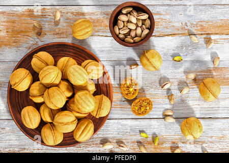 A forma di noce biscotti dolci ripieni con latte condensato e un trito di pistacchi di Bronte sul piatto di argilla sulla vecchia vernice peeling plance, vista da sopra Foto Stock