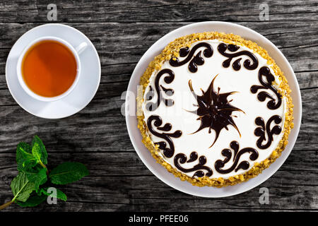 La deliziosa torta di pan di spagna con il miele e le prugne secche, stratificata con mantecato di panna, decorata con glassa di cioccolato, sul vecchio scuro listoni in legno con tazza di Foto Stock