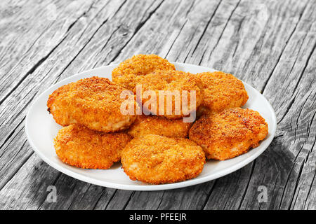 Close-up di succosa delizioso pollo impanato cotolette sulla piastra bianca su una vecchia tavola in legno rustico, vista da sopra Foto Stock