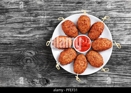 Succosa deliziosa carne alla brace cotolette su spiedini di bambù sulla piastra bianca con salsa di pomodoro in centro, sul vecchio scuro schede rustico, vista da sopra, copia Foto Stock
