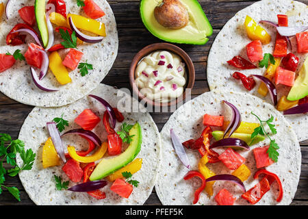 Deliziosa sano fajitas fatti in casa con i pezzi di salmone affumicato, fette di avocado, peperone, cipolla e prezzemolo con panna acida in piccolo vaso di creta sul vecchio Foto Stock