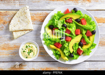 Salmone, Verde foglie di lattuga, fette di avocado e olive sane deliziosa insalata sul piatto bianco su vecchie tavole di legno con pita e salsa, visualizzare fr Foto Stock