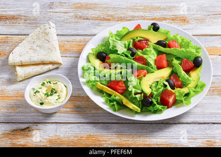 Salmone, Verde foglie di lattuga, fette di avocado e olive sane deliziosa insalata sul piatto bianco su vecchie tavole di legno con pita e salsa, visualizzare fr Foto Stock