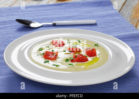 Una deliziosa zuppa cremosa purea con salmone affumicato cosparsa di prezzemolo in bianco ampio cerchio della piastra sulla tabella MAT con cucchiaio, vista da sopra, close-up Foto Stock