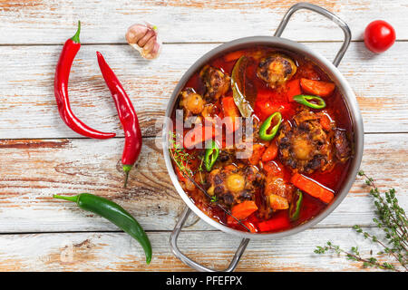 Rabo de toro o coda di vitellone stufato nel recipiente di cottura, peperoncino, aglio e timo sul vecchio tavolo in legno e tradizionale cucina andalusa, autentica ricetta, vista Foto Stock