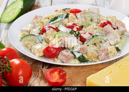 Una sana insalata con carne, cetriolo, pomodoro, formaggio, omelette tagliata in strisce e fette di mela con yogurt senape medicazione sulla piastra bianca con ingrediente Foto Stock