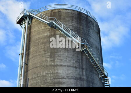 Alti calcestruzzo industriale silo circolari in acciaio con scale up lungo la parete che conduce alla piattaforma sulla parte superiore. Foto Stock