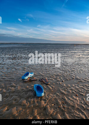 Scarpe blu a sinistra sulla sabbia a bassa marea su una spiaggia a Hayling Island, nel Hampshire, vicino a Portsmouth al tramonto Foto Stock