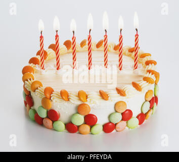 Torta di compleanno decorata con multi-colore di prodotti dolciari e di sette candele accese Foto Stock