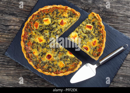 Torta salata di ricca crema di uova con spinaci e formaggio con tagliare una fetta sul vassoio di pietra con la spatola, vista da sopra Foto Stock