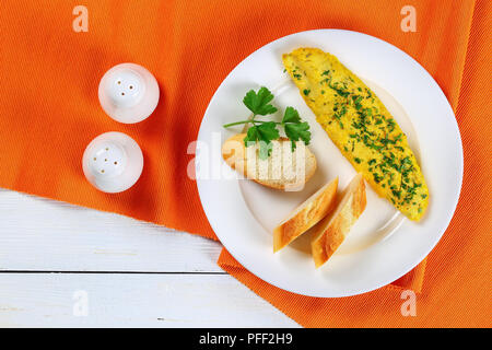 Deliziosa offerta francese frittata servita su piastra bianca con baguette fette e prezzemolo fresco, vista da sopra Foto Stock