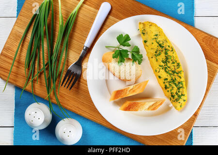 Delizioso francese di base offerta frittata servita su piastra bianca con baguette fette e prezzemolo fresco sul tagliere con il sale e il pepe e Foto Stock