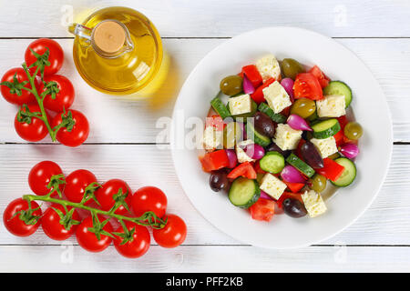 Deliziosa insalata greca con verdure fresche, il formaggio feta verde e olive kalamata, cipolla rossa lampadine su piastra bianca sul tavolo con maturi di pomodori ciliegini Foto Stock