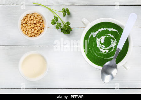 Una sana deliziosa crema di spinaci-zuppa con panna acida in doppia gestite Soup Bowl con cucchiaio, sulla vecchia cucina bianca tabella con i pinoli in un piccolo recipiente, Foto Stock